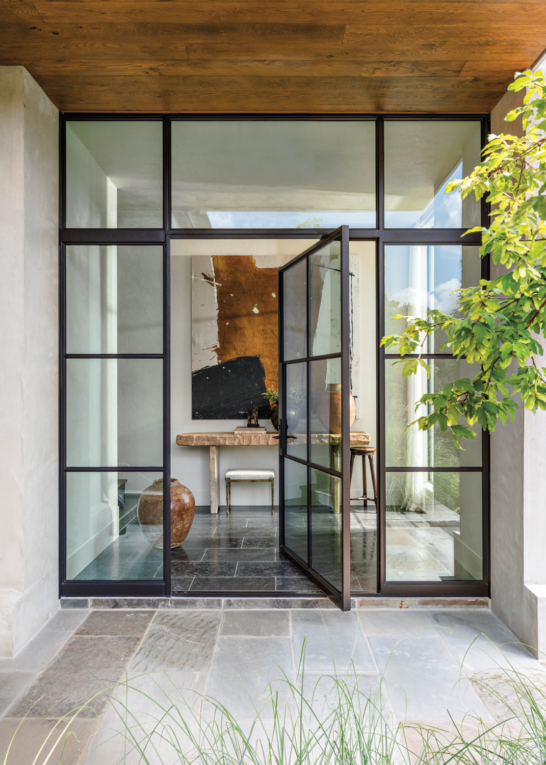Black framed divided-lite glass entry door opening onto a paved garden path