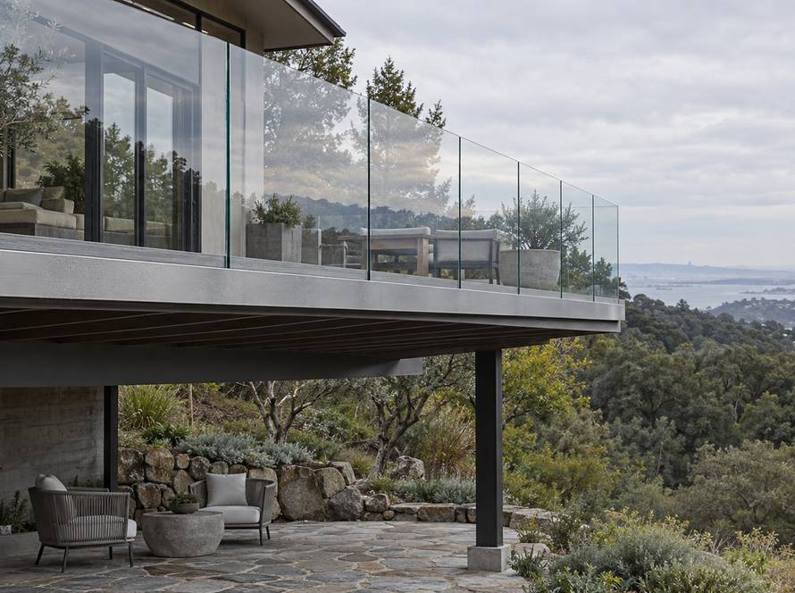 Frameless glass railing fascia-mounted on an elevated deck above a stone patio in the Bay Area