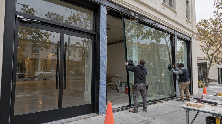 Glaziers installing an insulated glass unit in a black aluminum commercial storefront frame on a Bay Area street